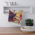 Colorful towel with a tea-themed design hanging on a white shelf above a wooden surface with a basket of bread.