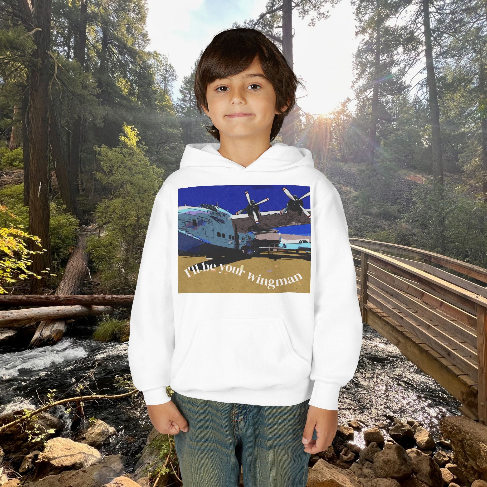 Child wearing a hoodie with an airplane graphic and text, standing in a forest setting.