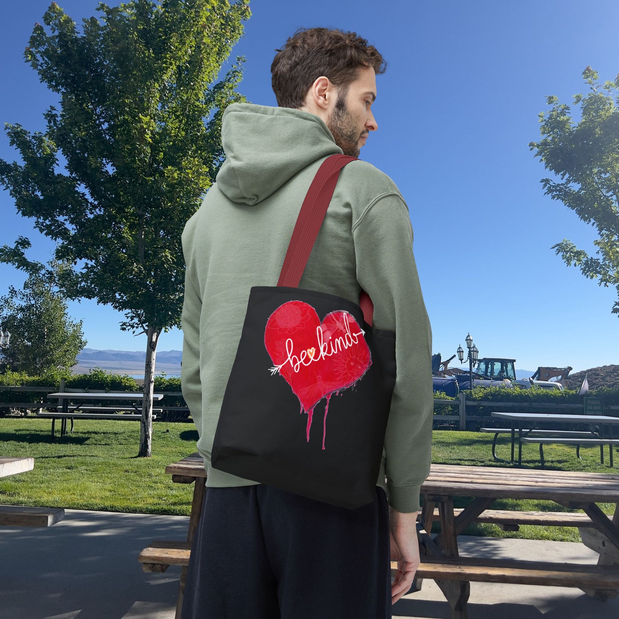 Person wearing a green hoodie with a red and black bag featuring a heart design outdoors.