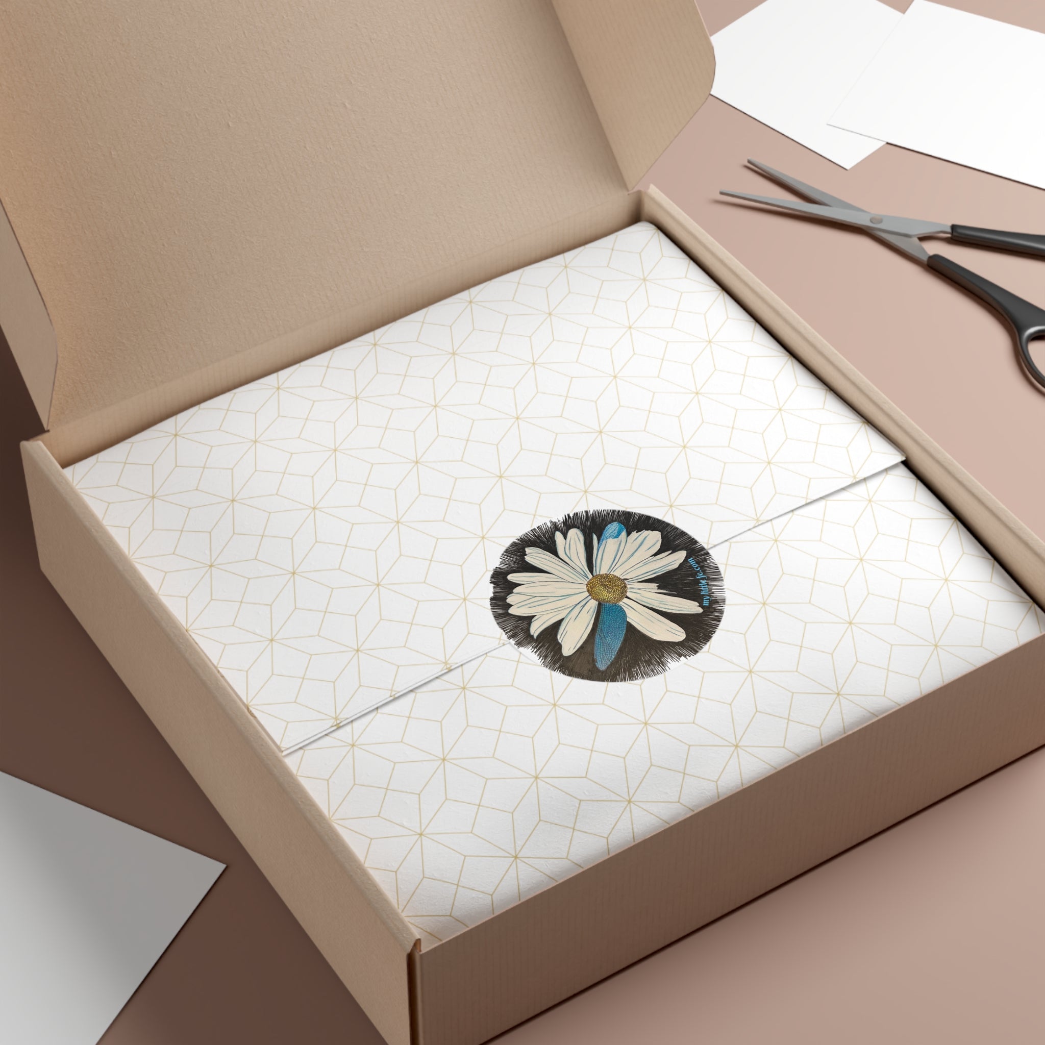 Open box with a round sticker of a daisy with dragonfly petals design on a black background on a textured surface