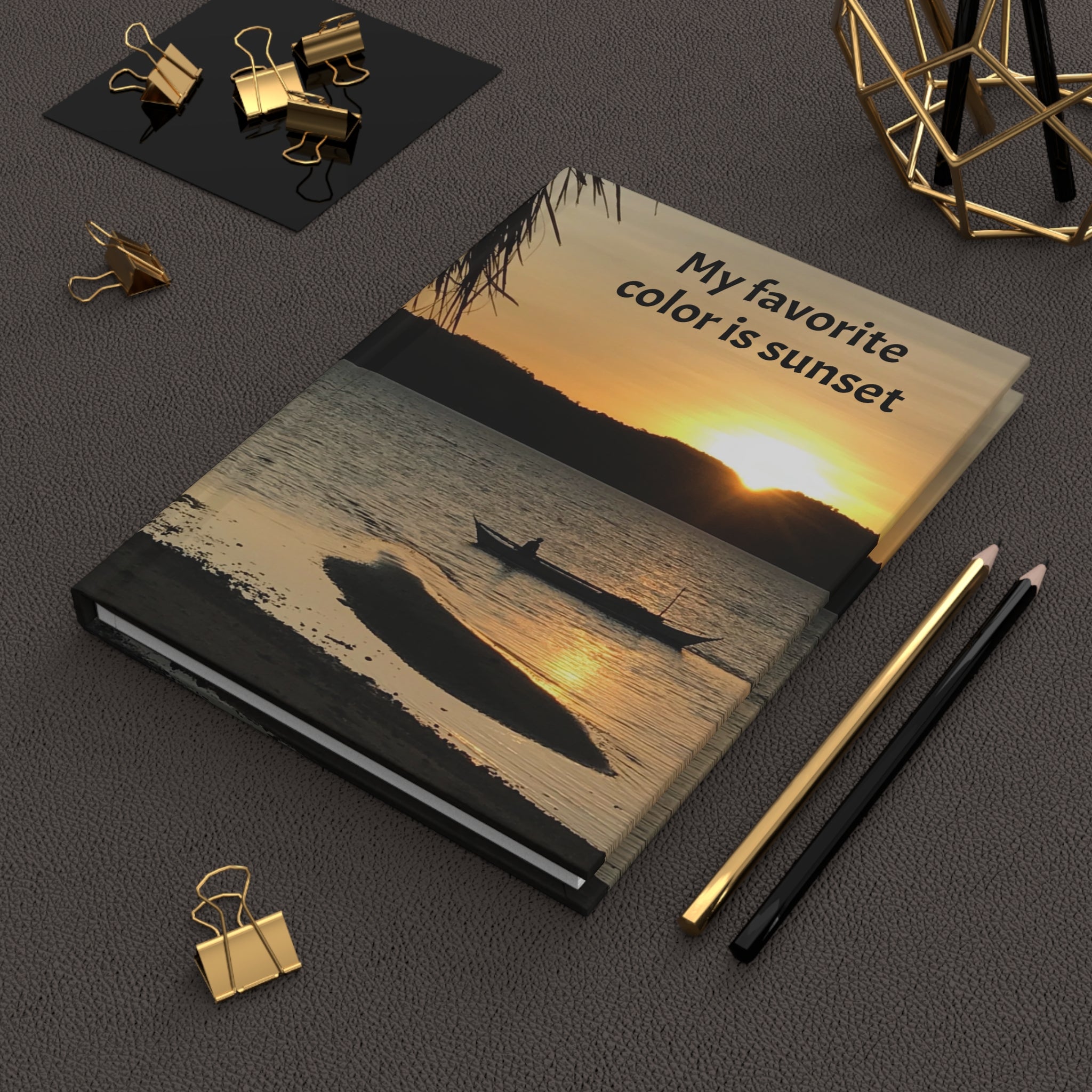 Notebook with sunset design and text 'My favorite color is sunset' on a dark surface with office supplies.
