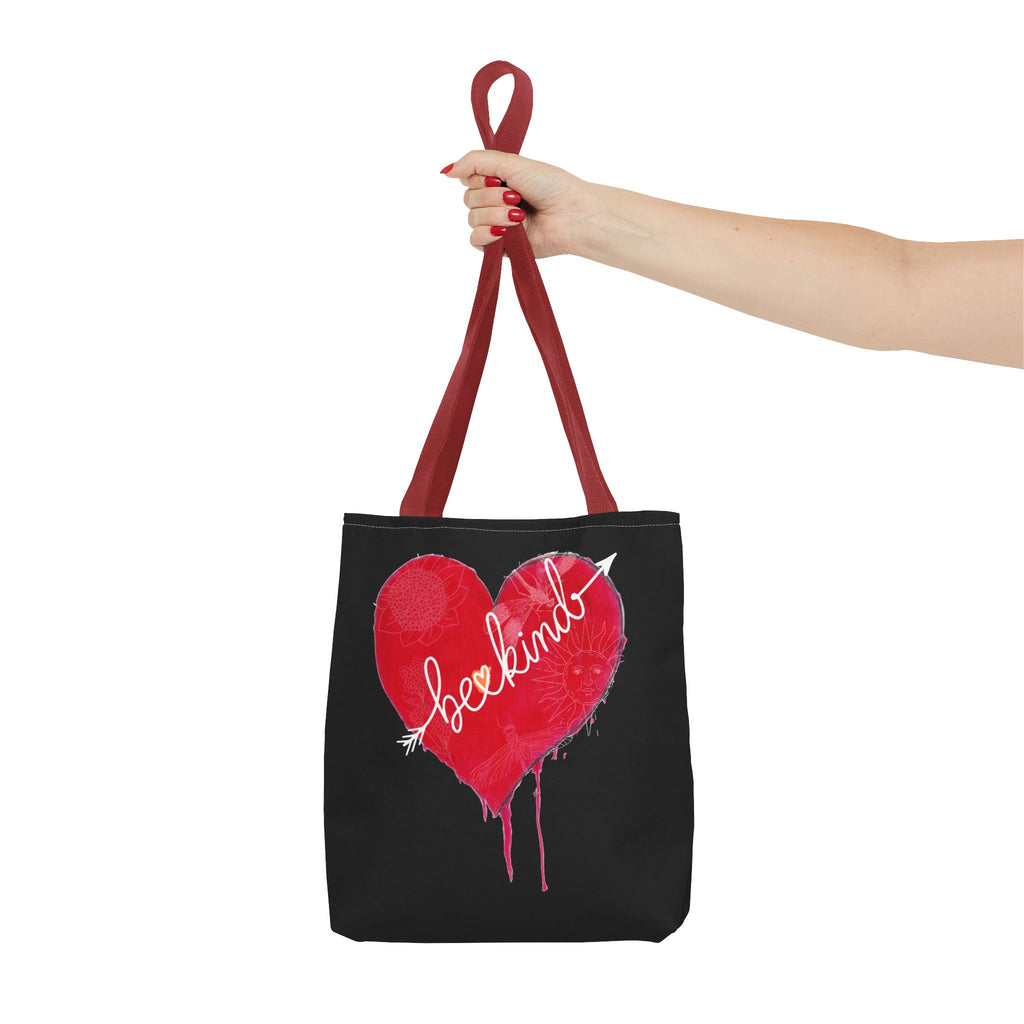 Black tote bag with a red heart and 'be kind' text held by a hand on a white background