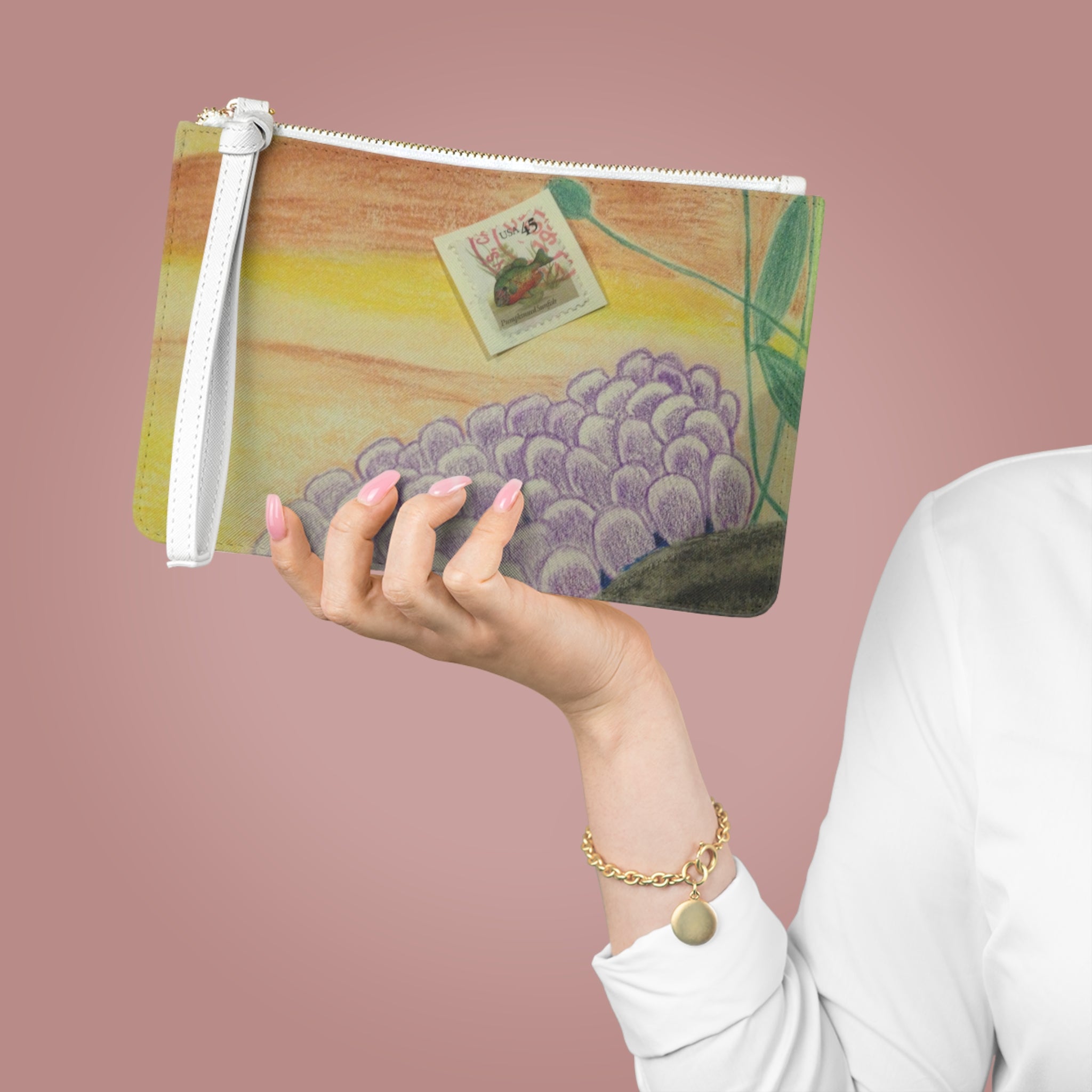 Hand holding a pouch with a painting of grapes and a postcard on a pink background