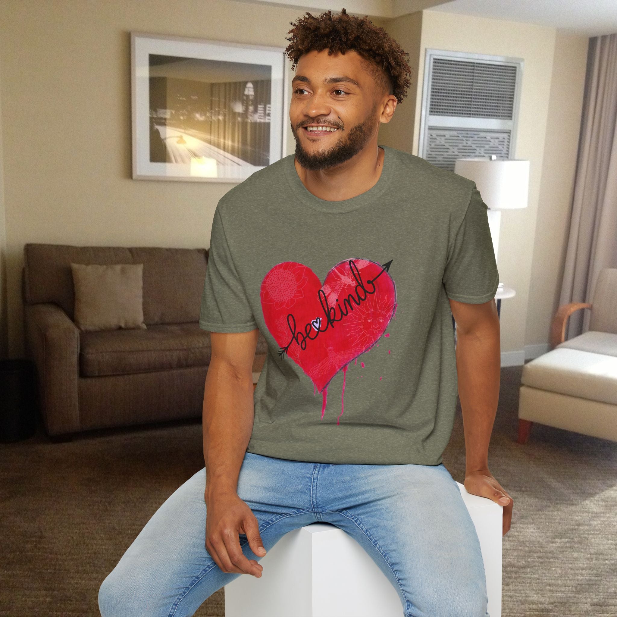 Man wearing a green t-shirt with a red heart design sitting in a living room.