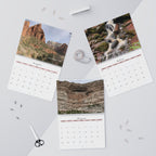 Calendar with scenic landscapes on a light gray surface with office supplies.