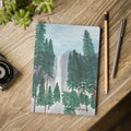 Notebook with forest design on a wooden surface with a pen and pencil.