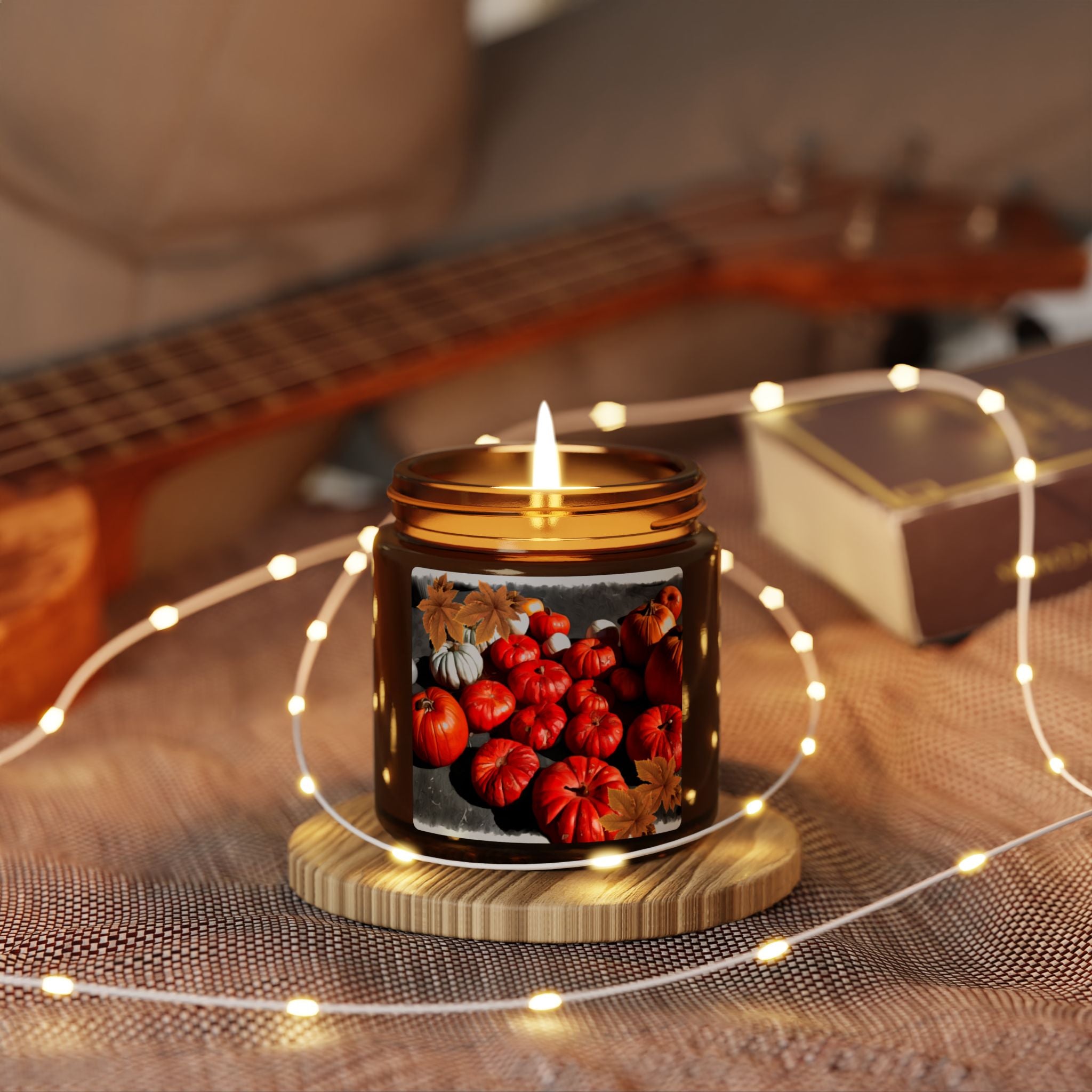Candle with pumpkin design on a wooden coaster surrounded by string lights, with a guitar in the background.