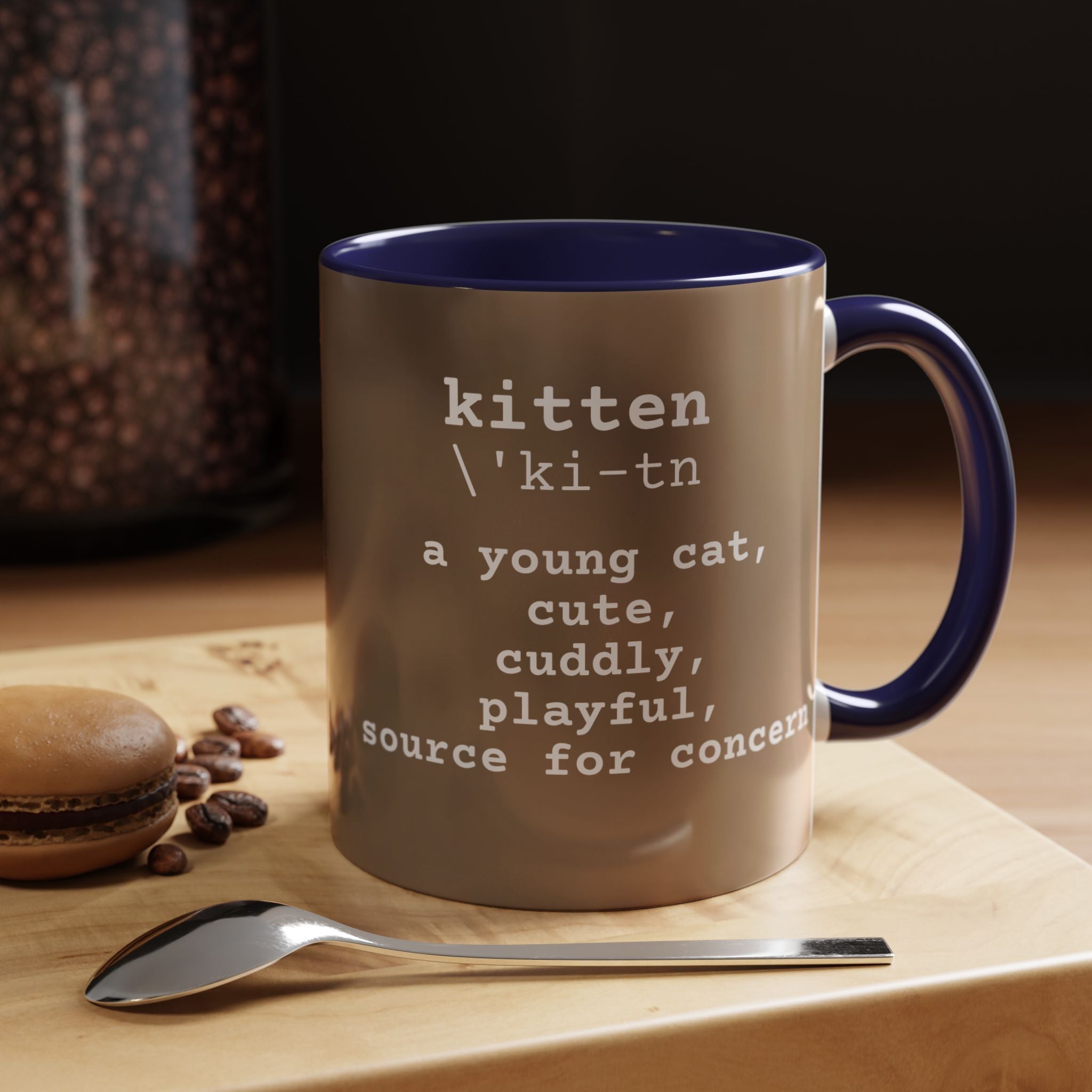 Mug with 'kitten' definition text on a wooden surface with coffee beans and a spoon.