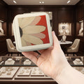 Hand holding a small rectangular jewelry box with a floral design against a jewelry store backdrop