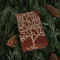 Brown notebook with beige leaf pattern on green pine needles and pine cones