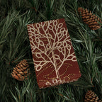 Brown notebook with beige leaf pattern on green pine needles and pine cones