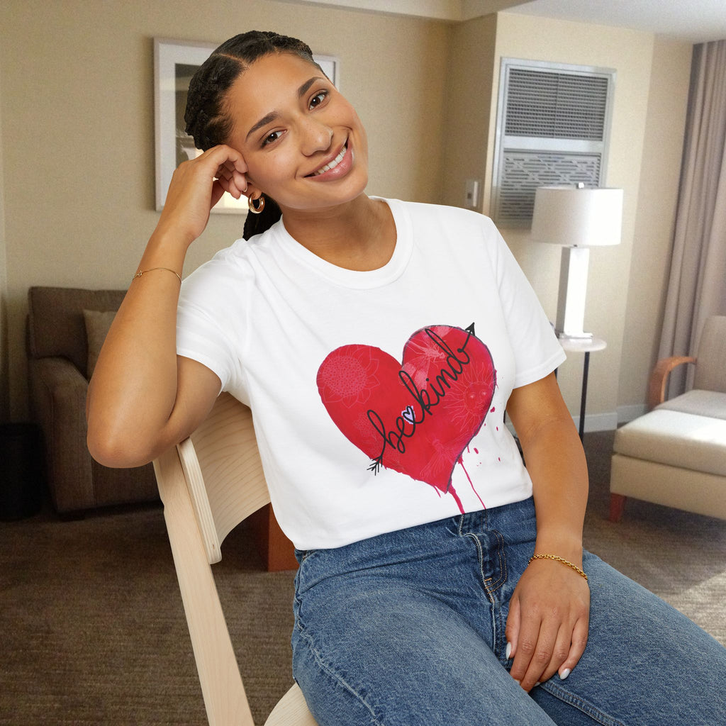 Woman wearing a white t-shirt with a red heart be kind design sitting in a room.