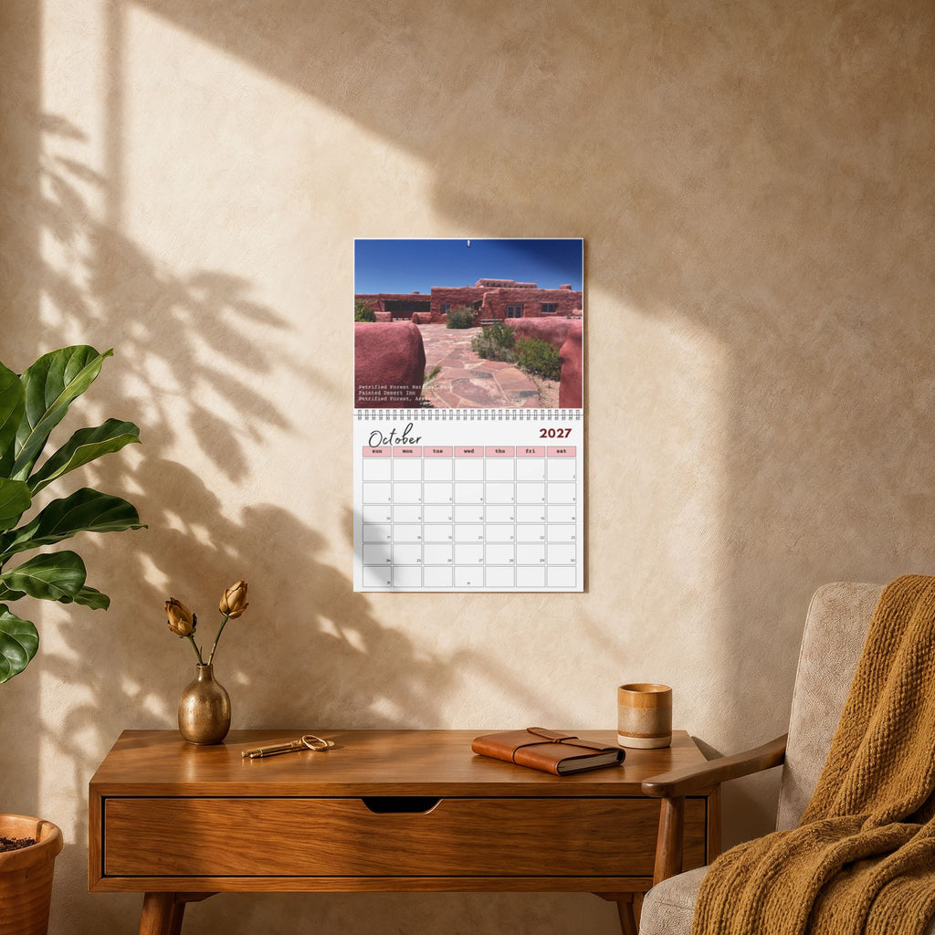 A wall-mounted 2023 desk calendar showing a desert landscape photograph, styled in a warm, sunlit room on a wooden console table next to a chair with a brown throw blanket.