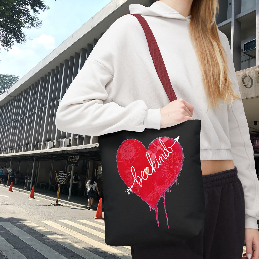 Person holding a black tote bag with a red heart design outdoors.