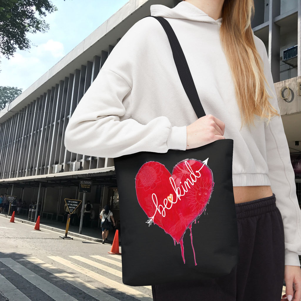 Person holding a black tote bag with a red heart design and text, standing on a street.
