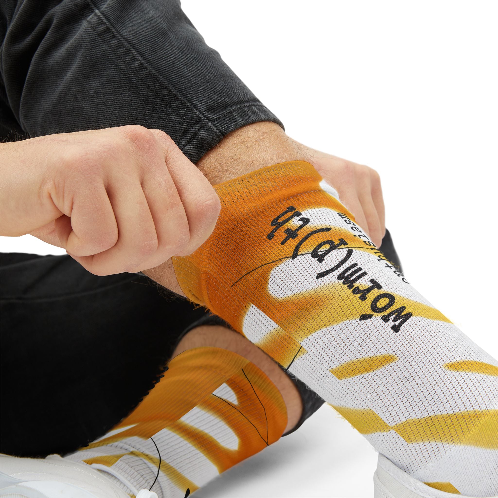 Person wearing orange and white socks with text, sitting on a white surface.