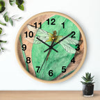 Wall clock with dragonfly design on a green background, placed on a wooden surface with a plant in the background.