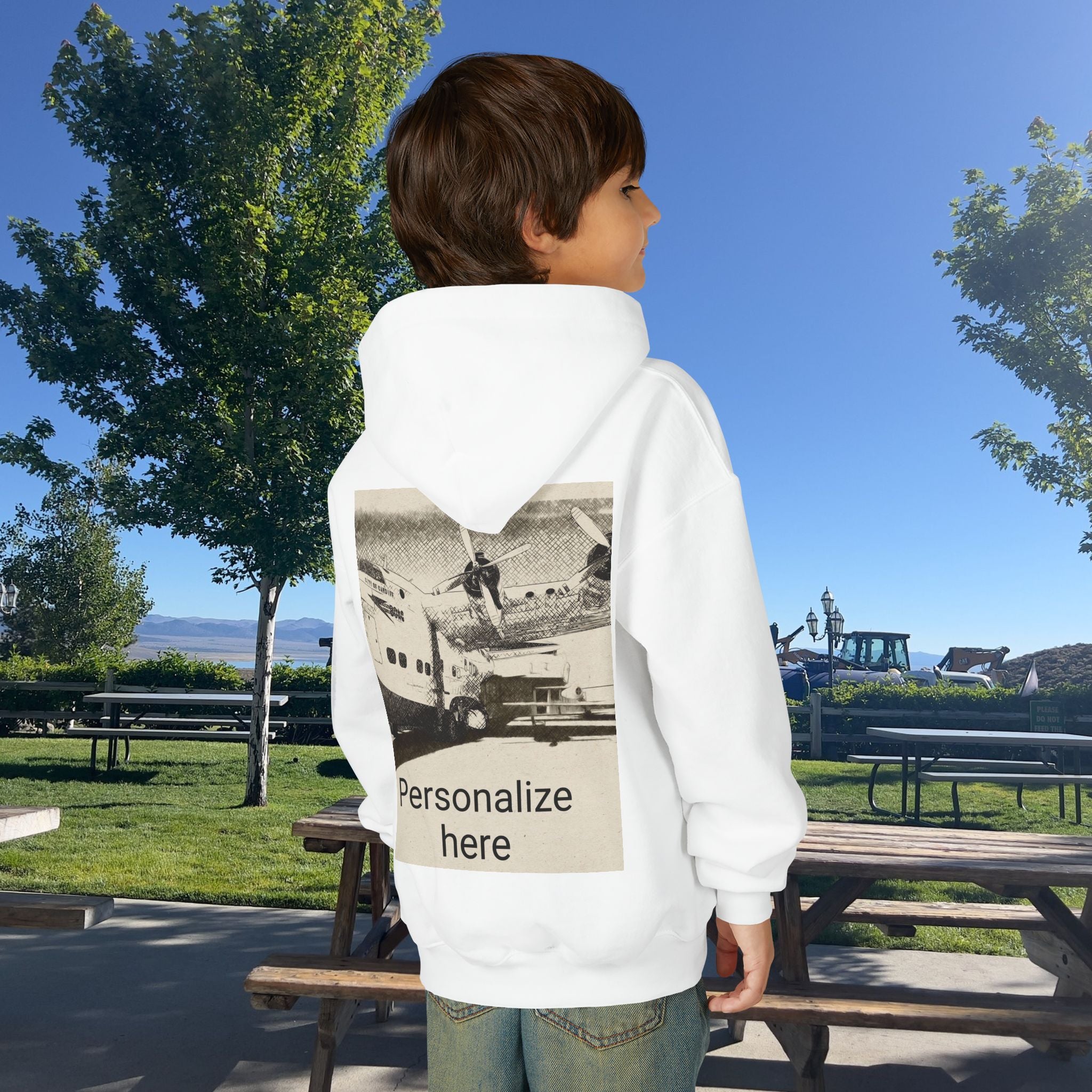 Child wearing a white hoodie with a printed design and 'Personalize here' text in a park setting.