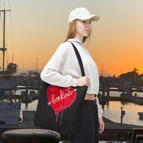 Woman holding a black tote bag with a red heart design at sunset by a marina.