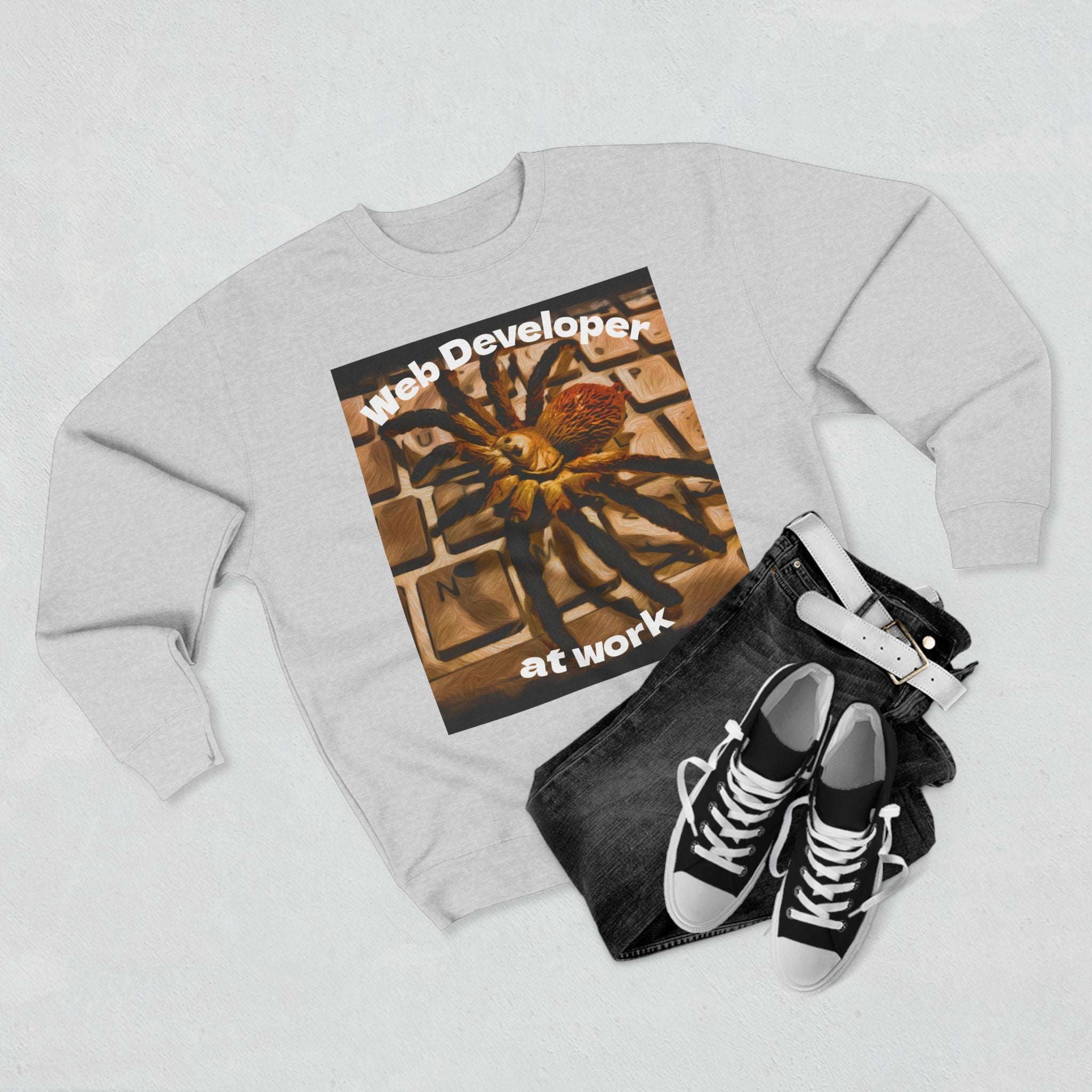 Sweatshirt with a spider on a keyboard design with text web developer at work and a pair of sneakers and black jeans next to it.