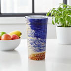 Tumbler with a colorful design on a kitchen counter with fruits and a plant.
