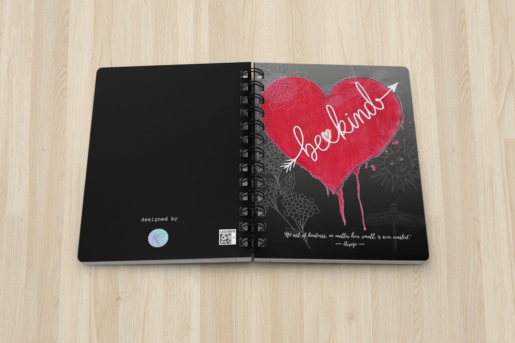 Spiral notebook opened with bleeding heart design and be kind text on top a birch desk