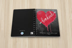 Spiral notebook opened with bleeding heart design and be kind text on top a birch desk
