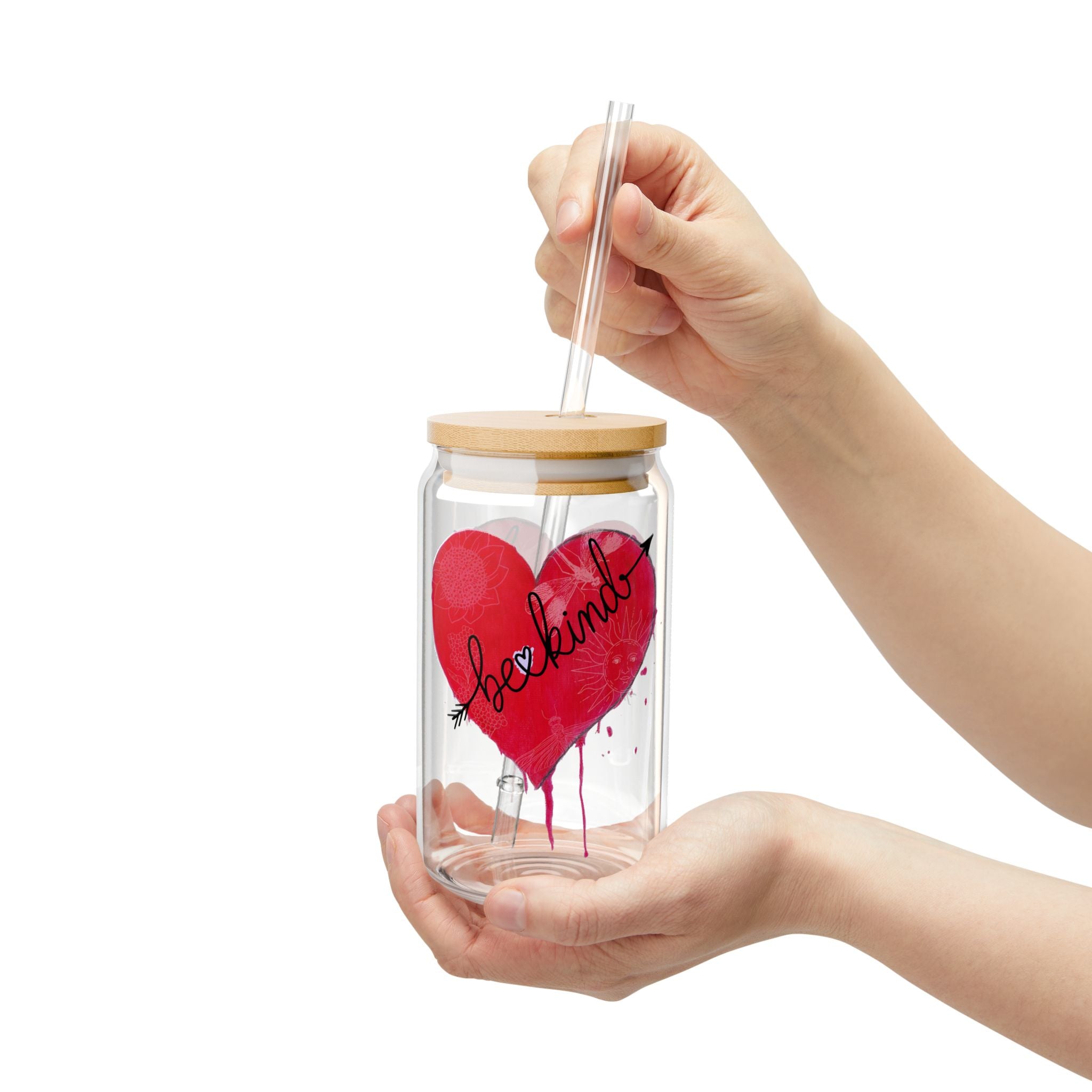 Glass jar with a red heart and 'be kind' text, held by hands on a white background