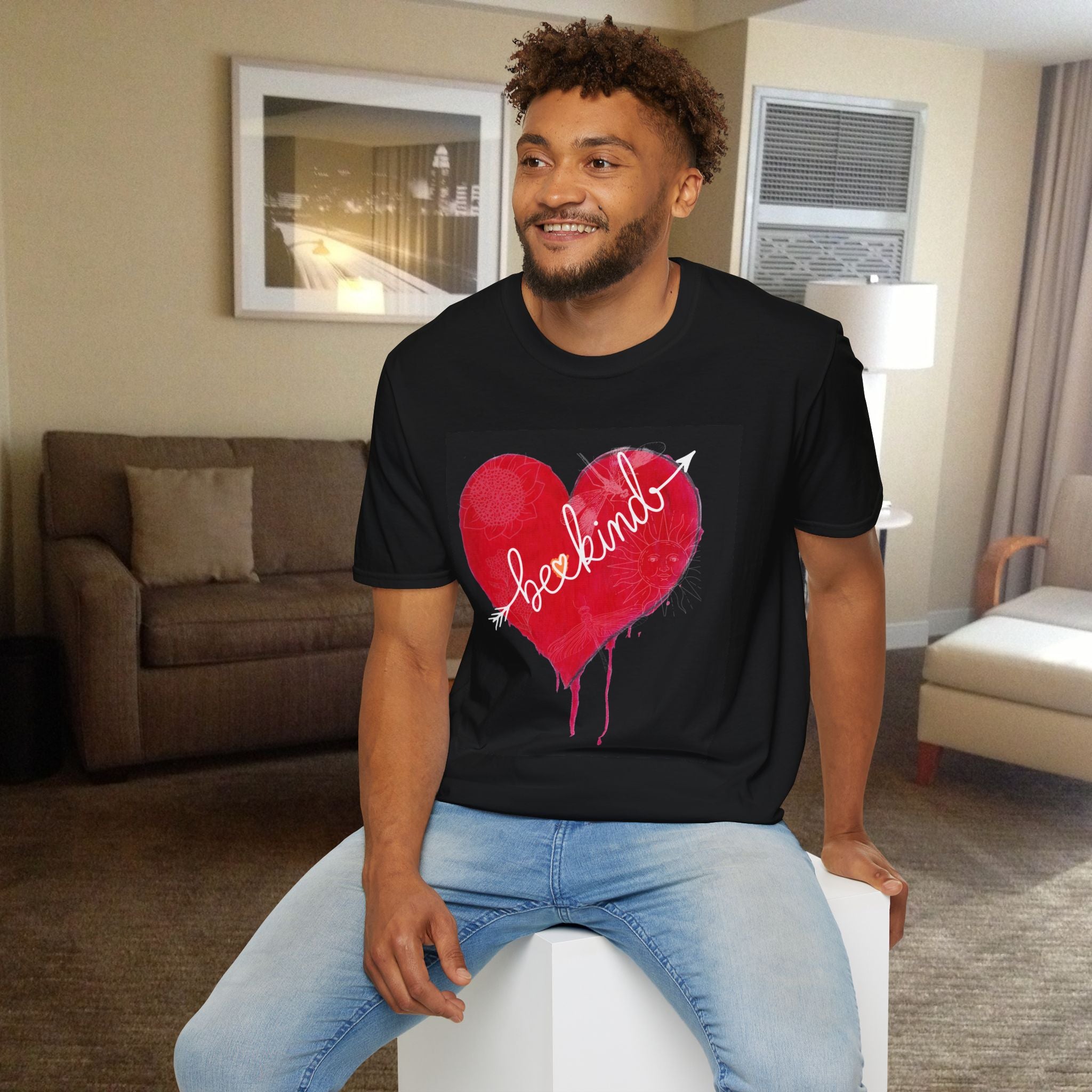 Man wearing a black t-shirt with a red heart graphic sitting in a living room.