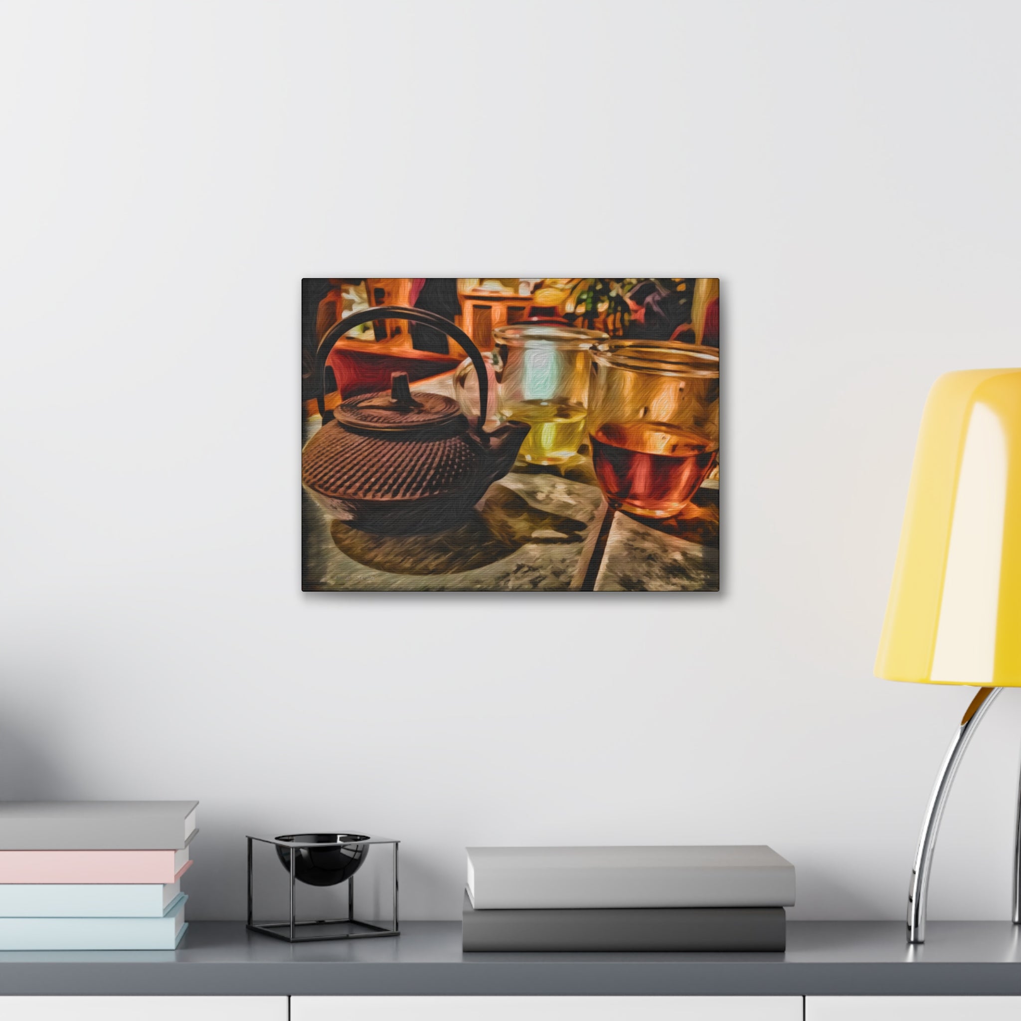 Canvas print of a teapot and glasses on a wall above a desk with books and a lamp.