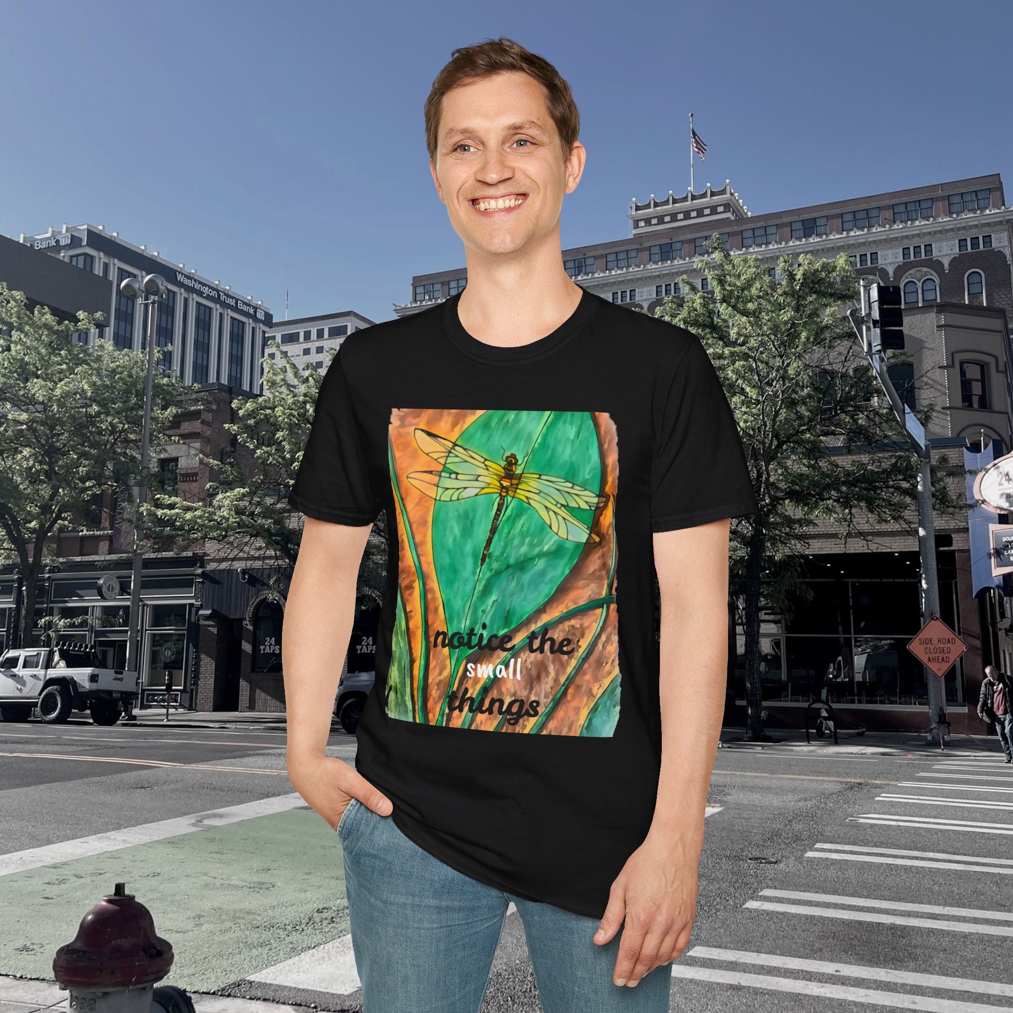 Person wearing a black t-shirt with a colorful dragonfly design and text, standing on a city street.