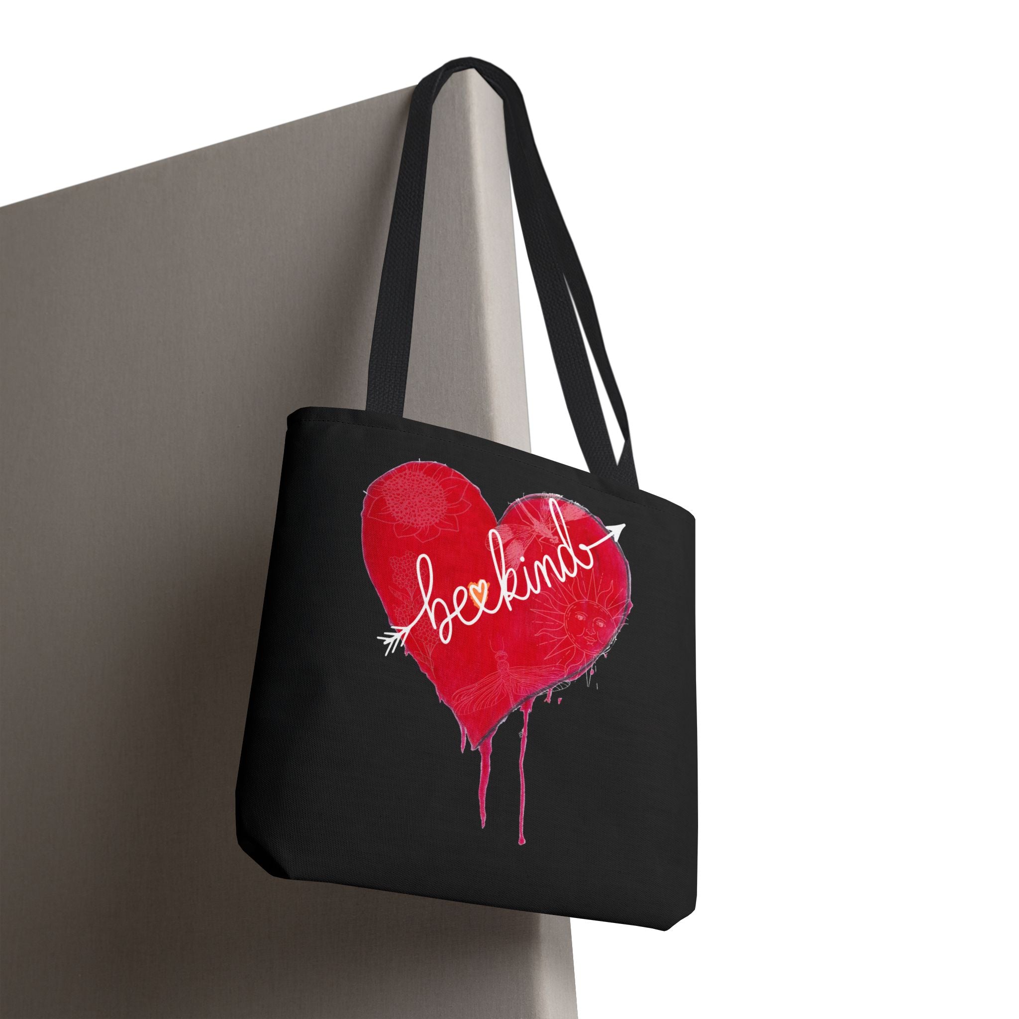 Black tote bag with a red heart and 'lovekind' text on a gray surface