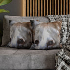Two dog face cushions on a sofa with a plaid blanket and wooden headboard in the background.