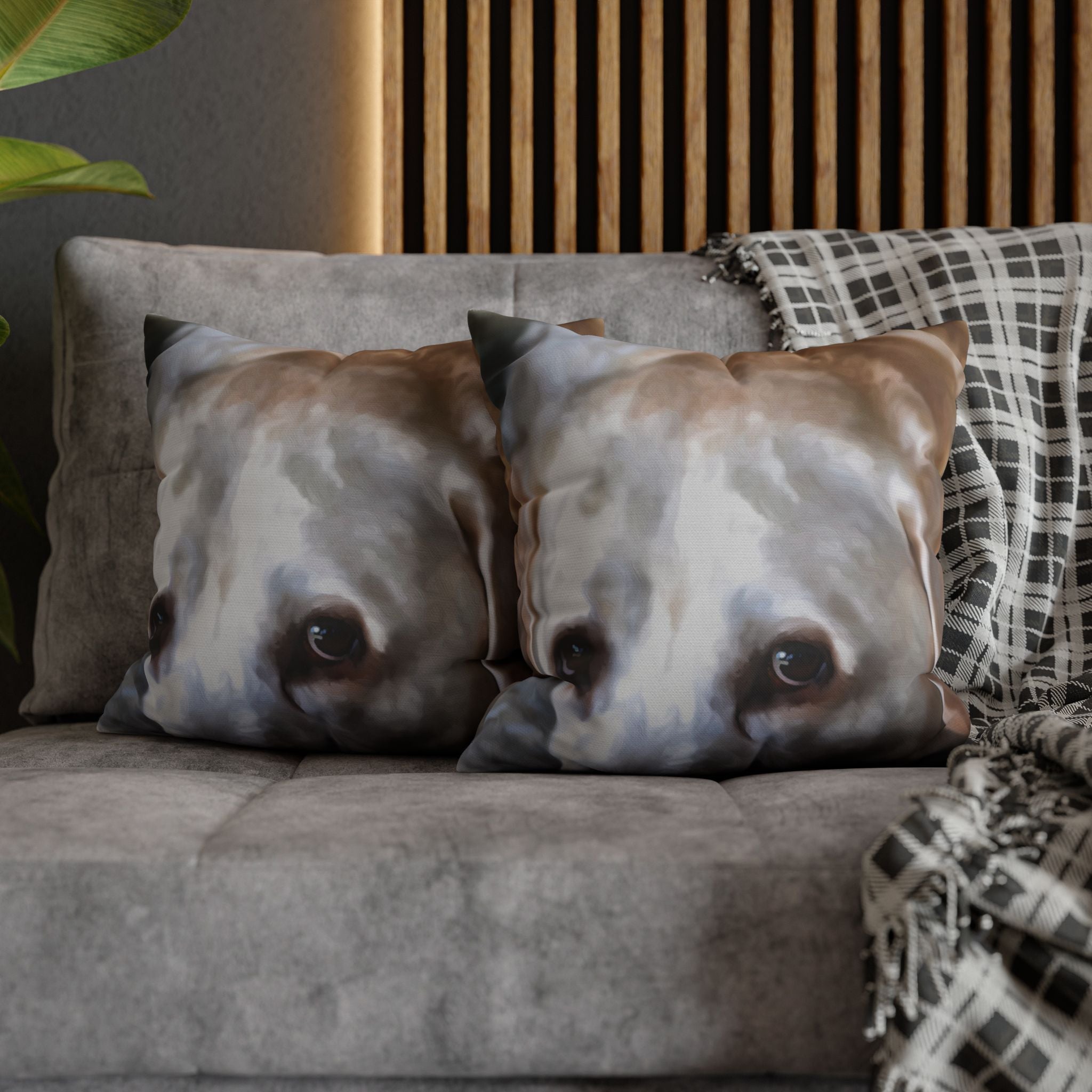 Two dog face cushions on a sofa with a plaid blanket and wooden headboard in the background.