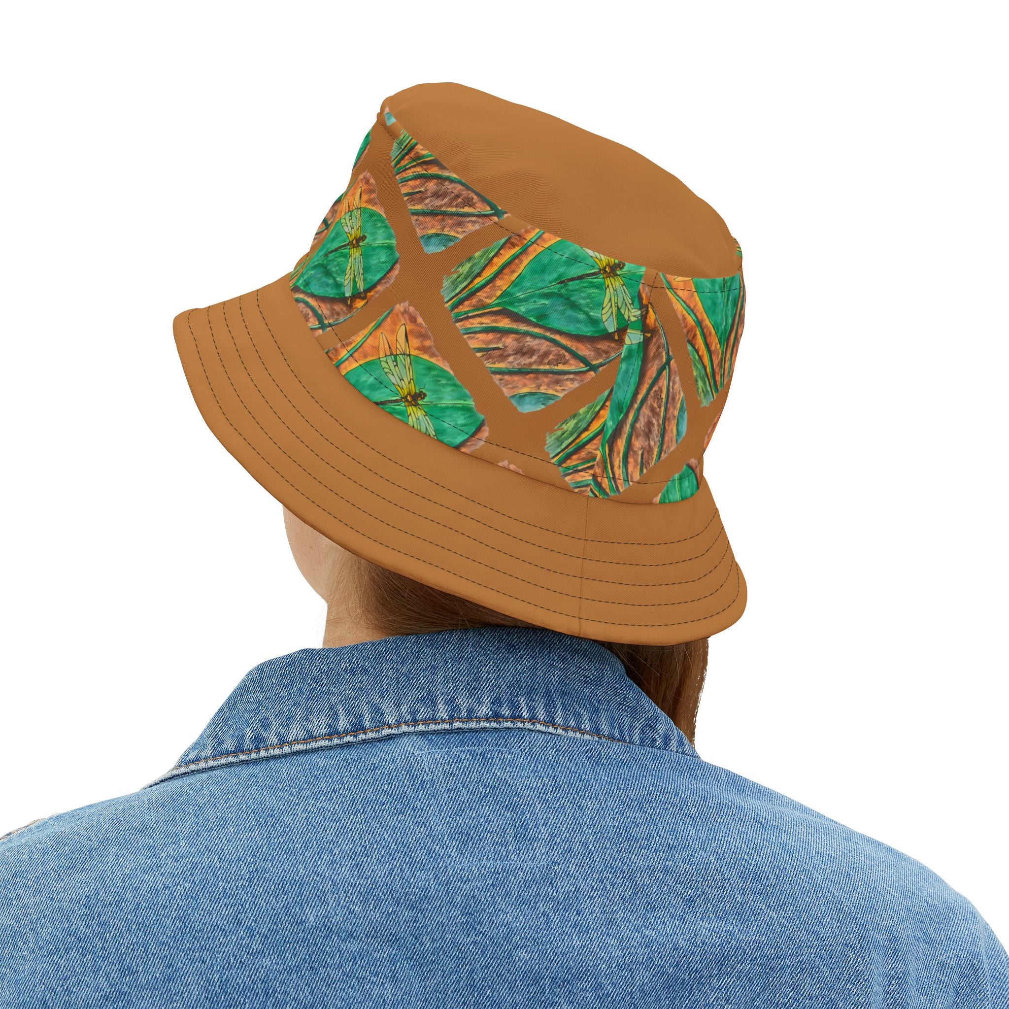 Person wearing a brown bucket hat backside with dragonfly on a green leaf pattern on a white background