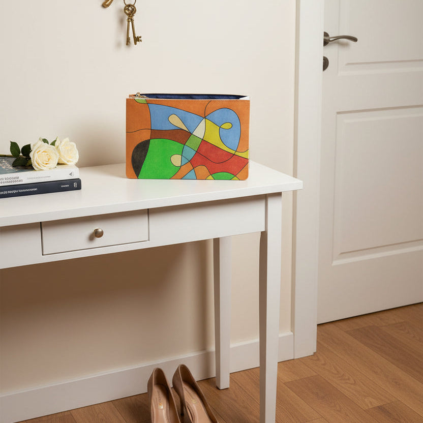 Clutch bag with Abstract design on a table by an entry door with a keyholder on the wall and shoes on the floor and books next to the bag.