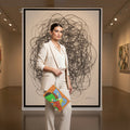 Clutch bag with a colorful abstract design held by a woman in front of a piece of artwork in a gallery