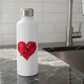 Red heart-shaped sticker with 'be kind' text and decorative elements  sitting on a kitchen counter by the sink.