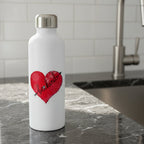 Red heart-shaped sticker with 'be kind' text and decorative elements  sitting on a kitchen counter by the sink.