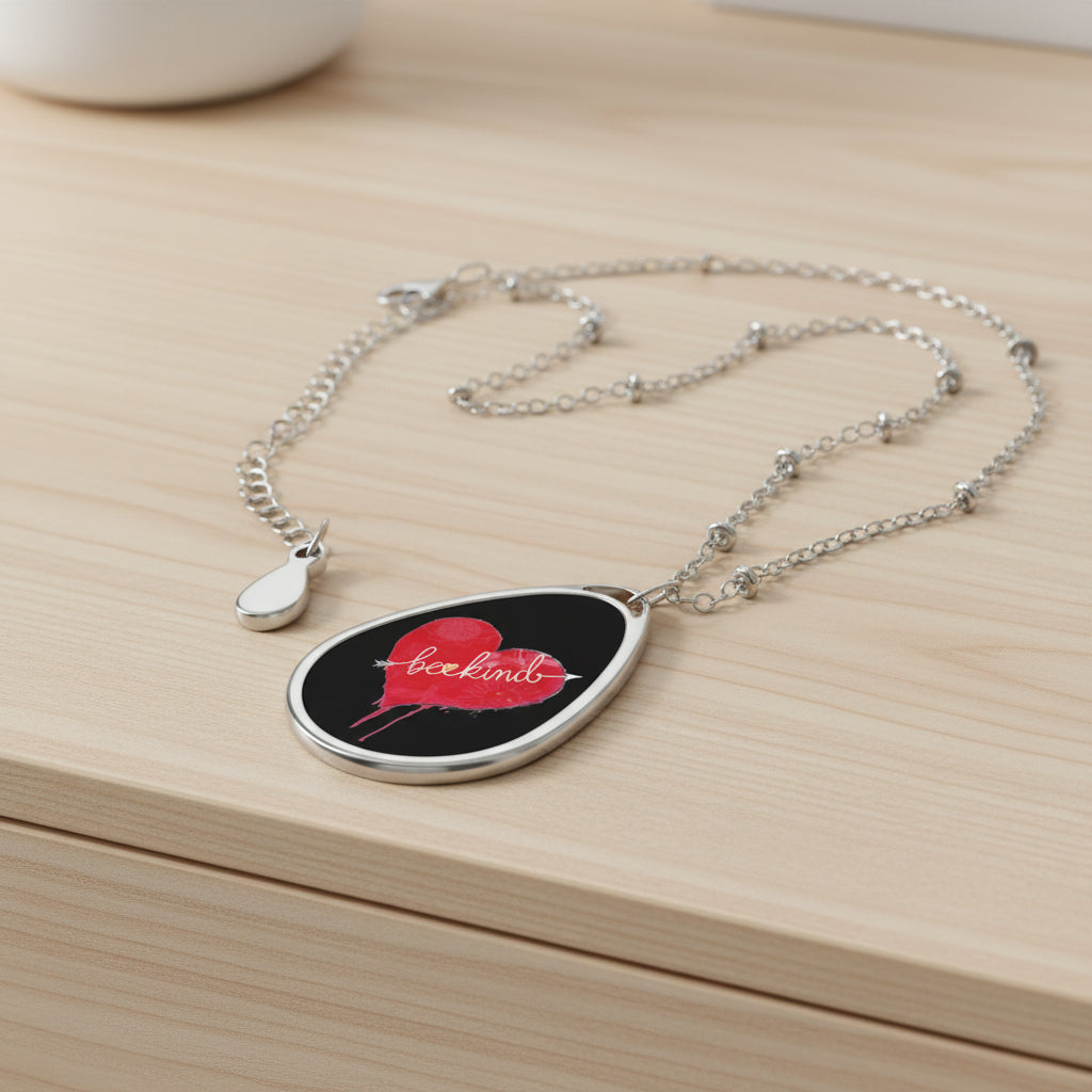 A silver teardrop-shaped pendant necklace featuring a black background with a red heart design and the word 'bookimb' in white script, displayed on a light wood dresser