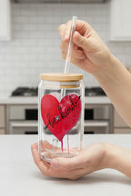 Glass jar with a red heart and 'be kind' text, held by hands with kitchen background
