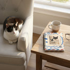 A spiral-bound notebook with a vintage airmail envelope design in red, white, and blue, featuring a central stamp-like graphic with a black-and-white cat photo and the words 'Cuteness Guaranteed'.