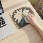 Laptop with a mouse pad featuring a daisy dragonfly wings design on a light wood desk with a woman's hand on the mouse