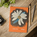 Notebook with a floral design and 'notice the small things' text on a wooden surface with a pencil and pen.