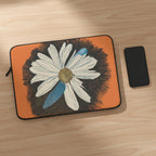 Laptop sleeve with a daisy dragonfly wings design on an orange background with phone next to it.