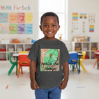A young child wearing a dark heather gray graphic t-shirt with a dragonfly and the text 'notice the things' on the front, paired with blue pants, in a pre-school setting