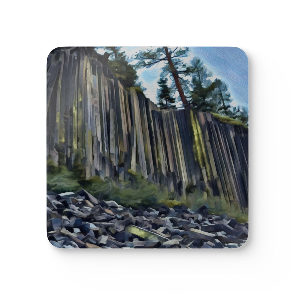 A square coaster with rounded corners featuring a painted landscape of a tall columnar cliff, green trees, and a blue sky, shown on a plain white background.