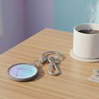 Keychain with a pastel-colored circular charm featuring a dragonfly design on a coffee table with a cup of coffee next to it.