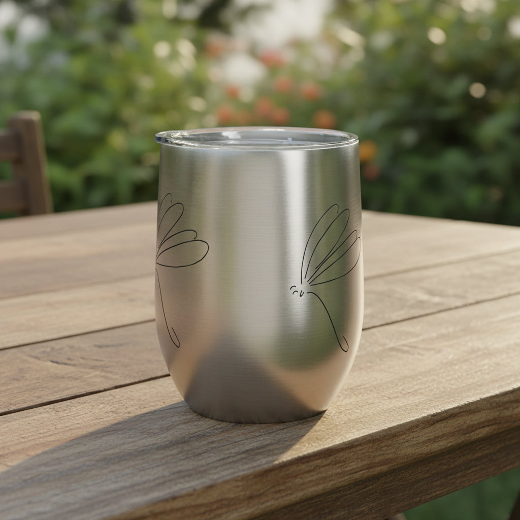Silver tumbler with dragonfly stick drawing on it's side showing half of the drawing on the other side sitting on a rustic outdoor dining table