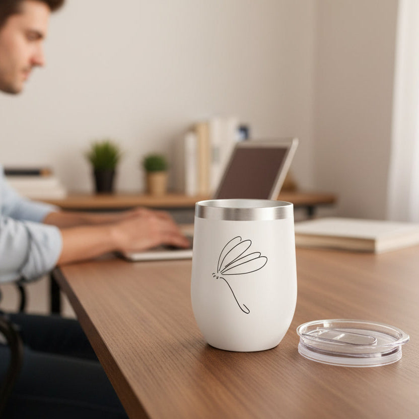 White Tumbler with simple Dragonfly stick drawing on a home office with a man working on his laptop in the background